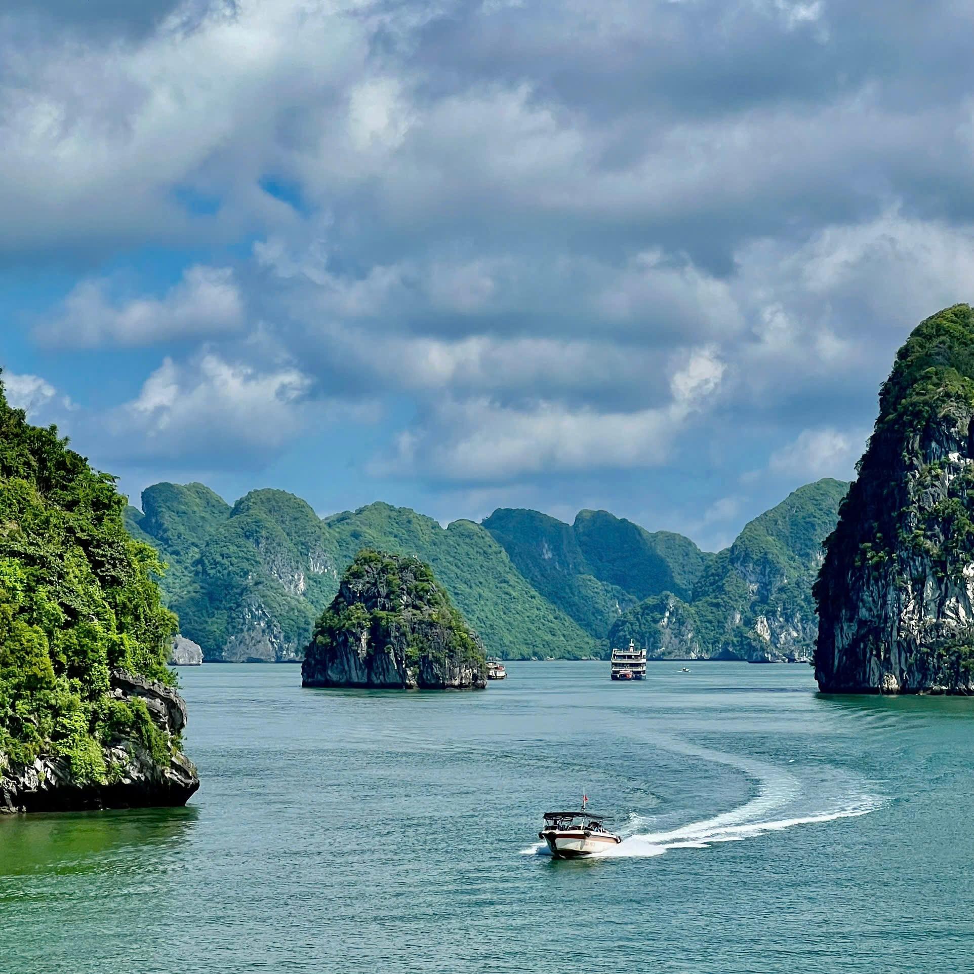 Limestone islands rising from green water with a boat leaving a wake behind it