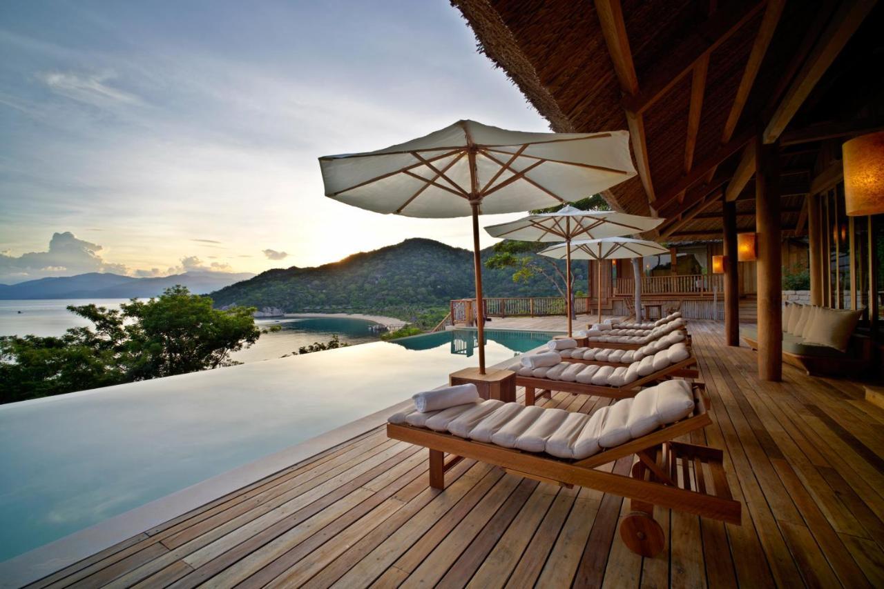 Sun loungers and parasols on a wooden deck beside an infinity pool above a bay