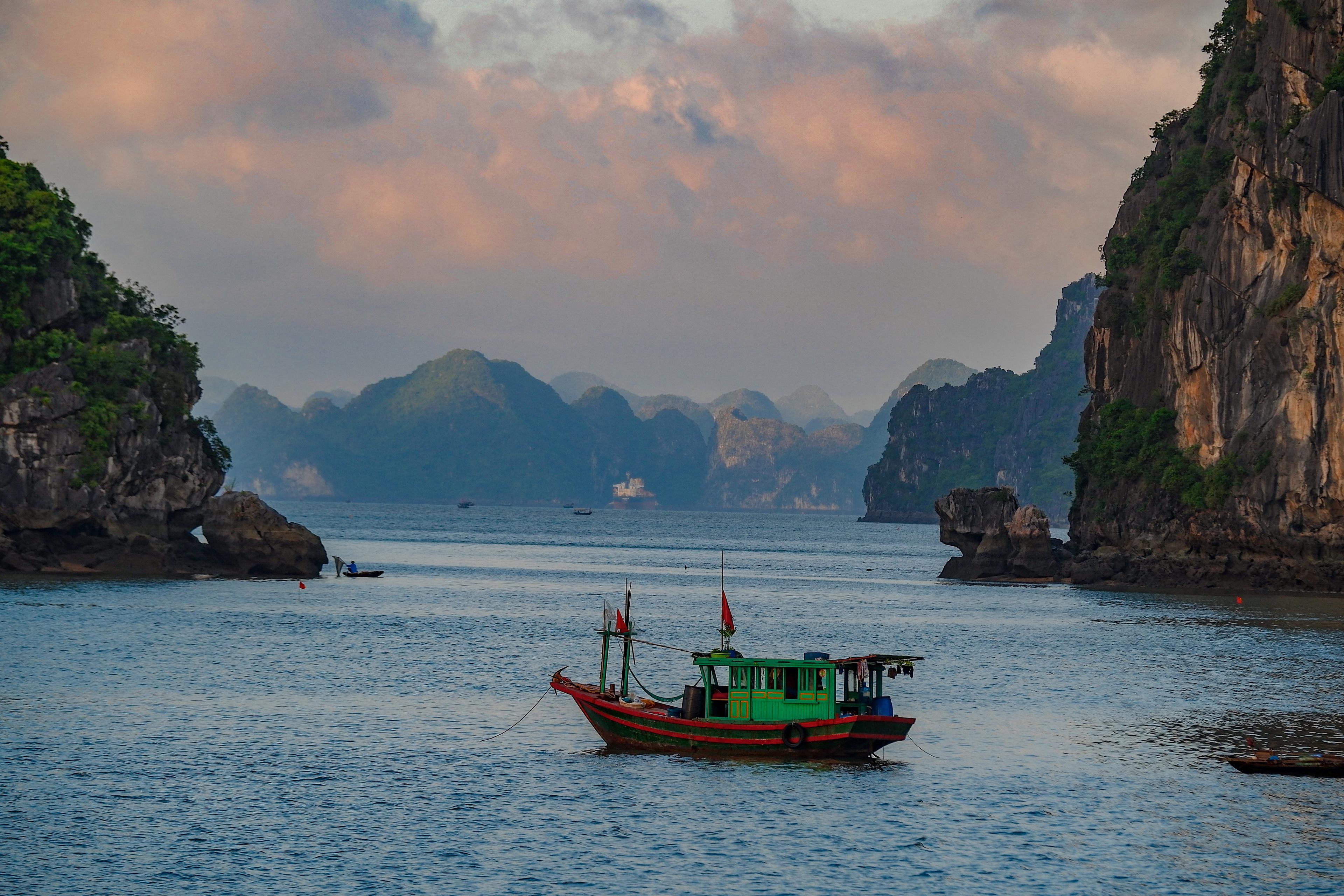 A wooden fishing boat on calm water below limestone karsts at dawn