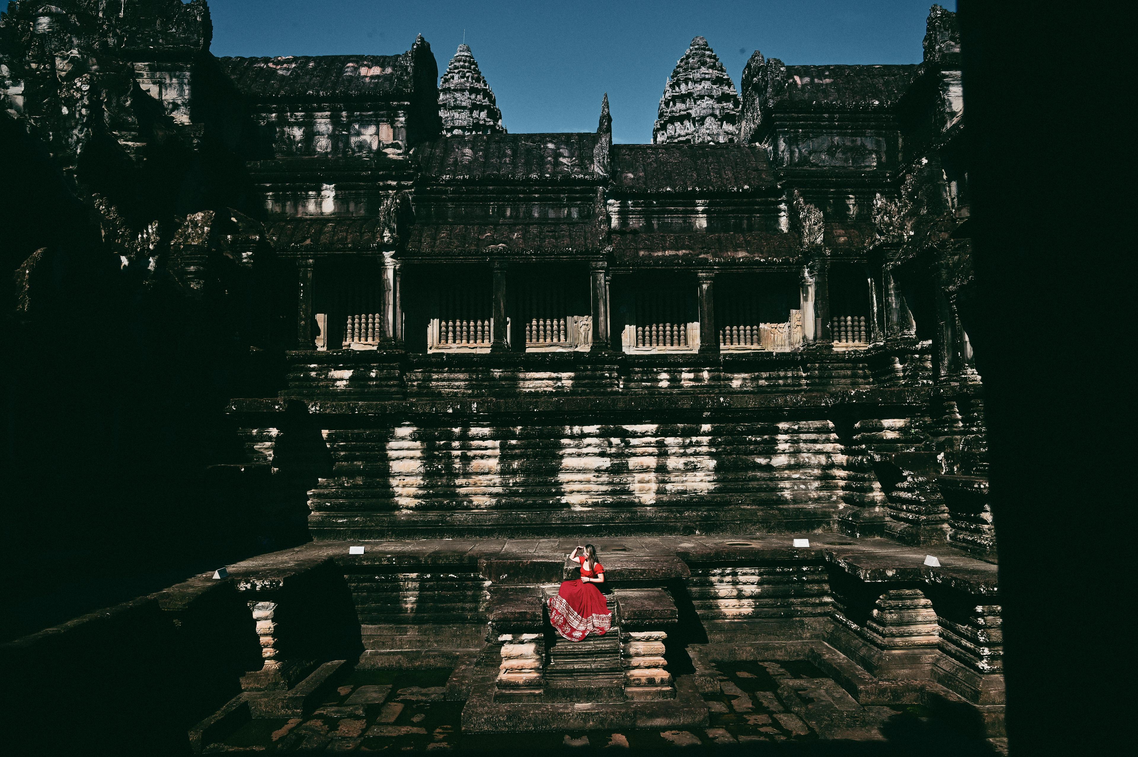 A woman in a red dress sitting alone in the stone courtyard of a temple