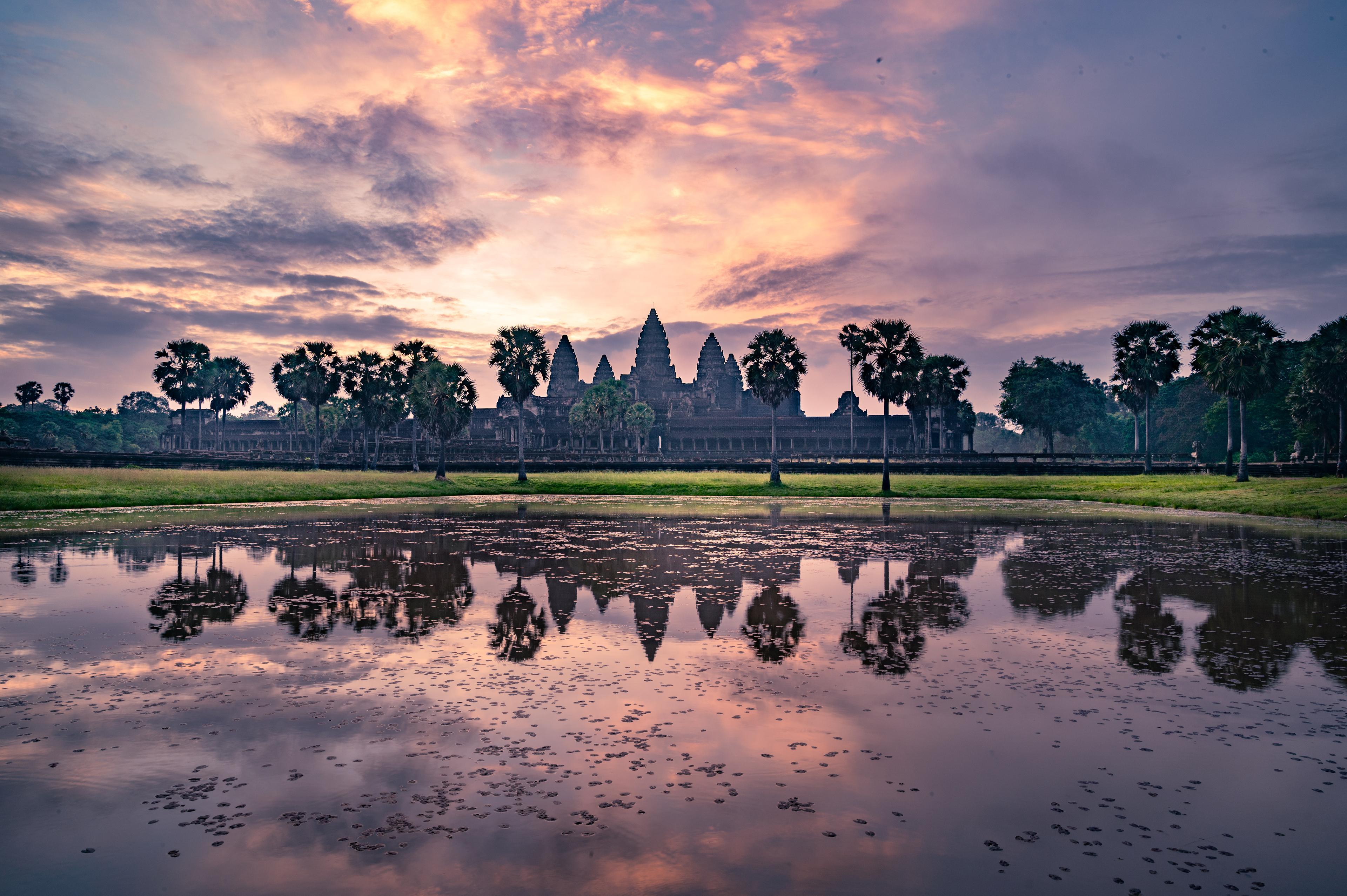 The towers of Angkor Wat reflected in still water at dawn