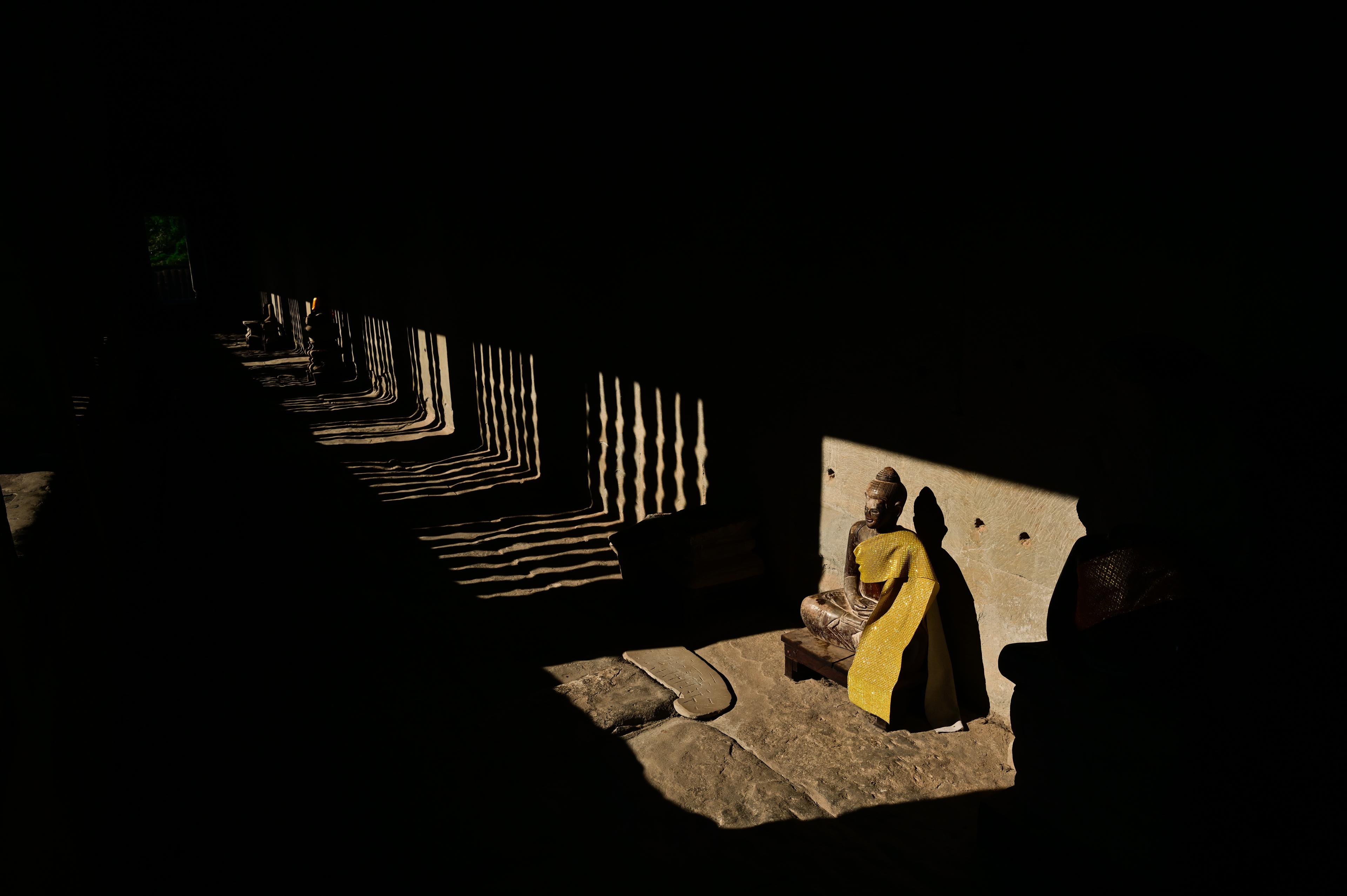 A Buddha statue draped in yellow cloth in a sunlit temple gallery