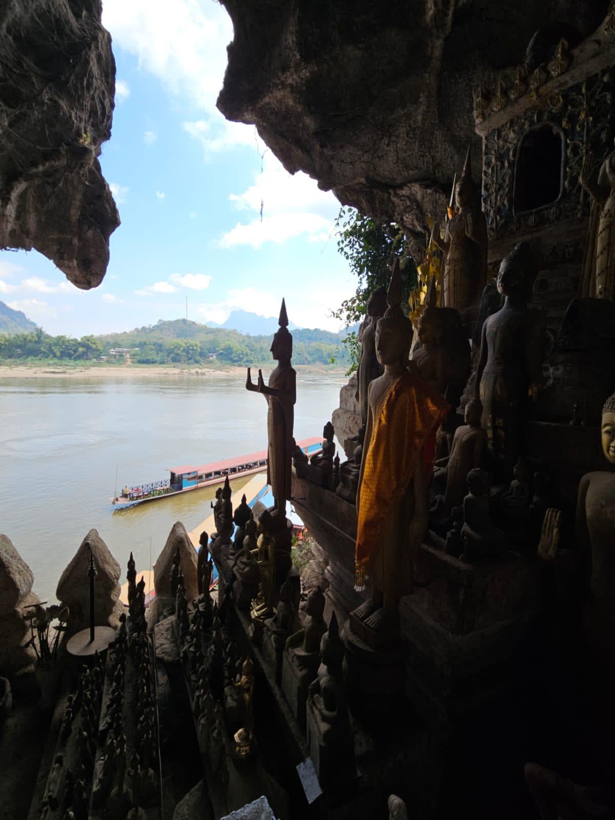 Buddha statues in a riverside cave looking out over the water and boats