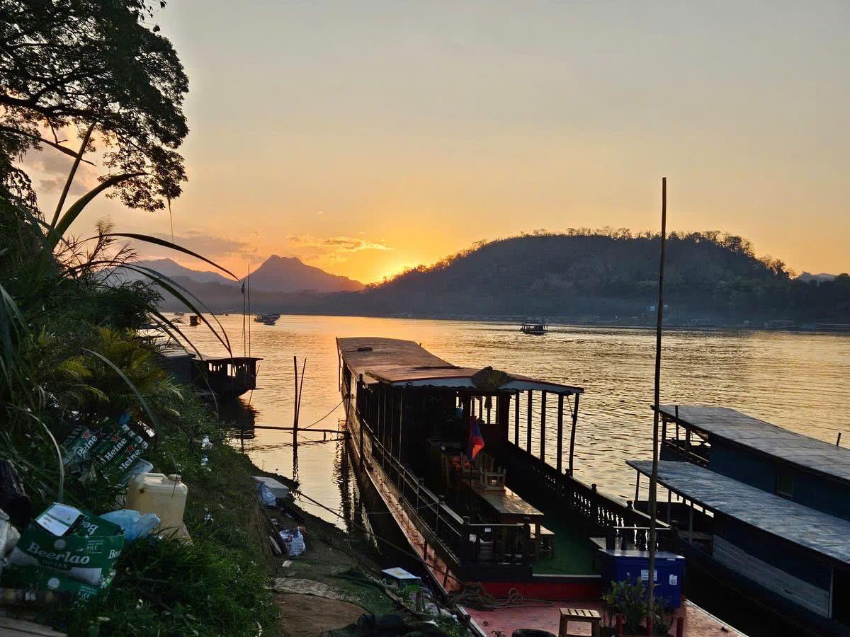 Wooden boats moored on the Mekong at sunset with hills across the water