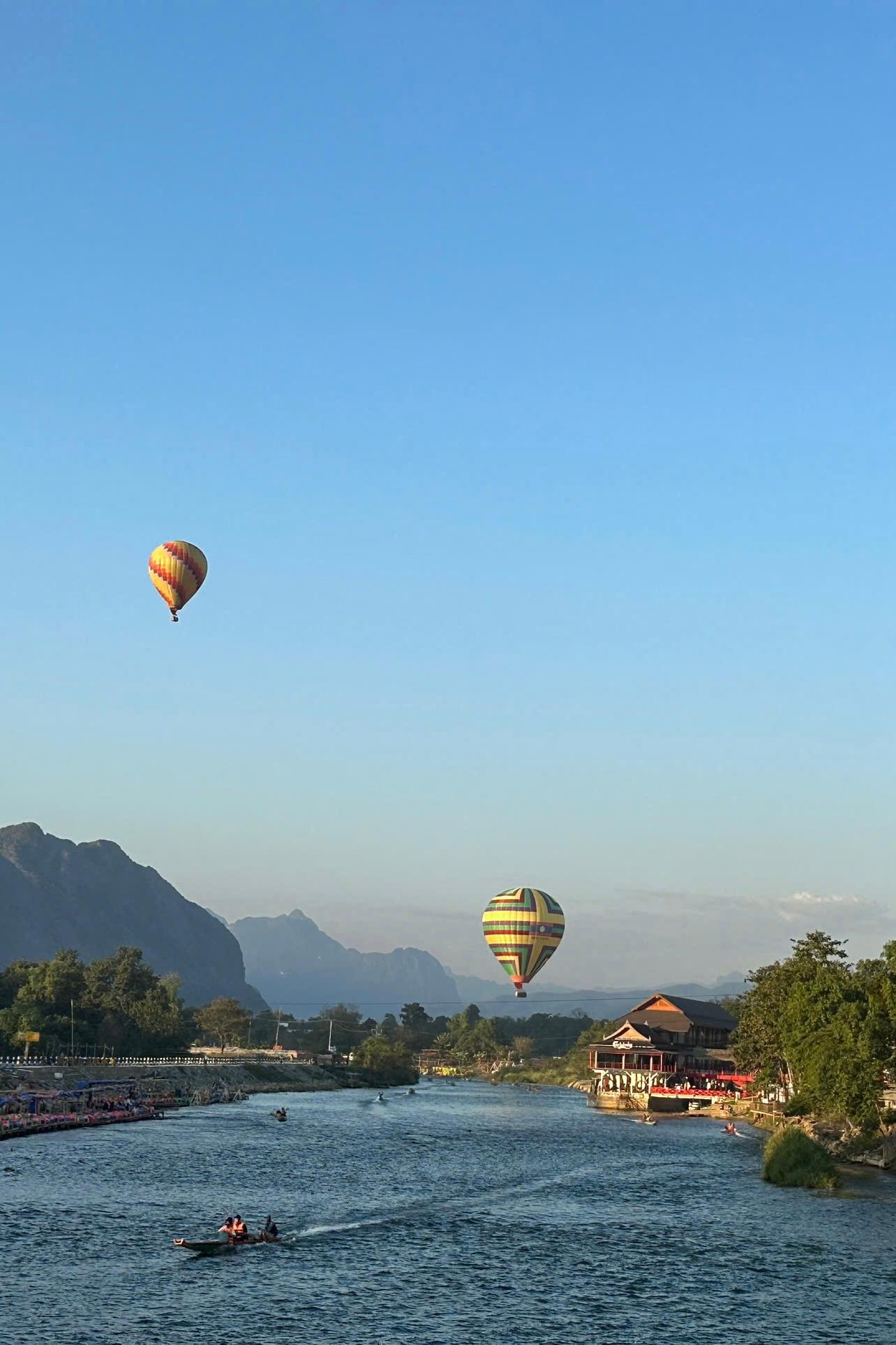 Two hot-air balloons drifting over a river valley ringed by limestone peaks