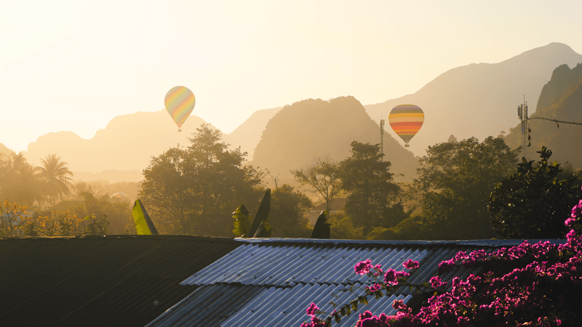 Hot-air balloons rising over misty limestone hills above a tin-roofed village