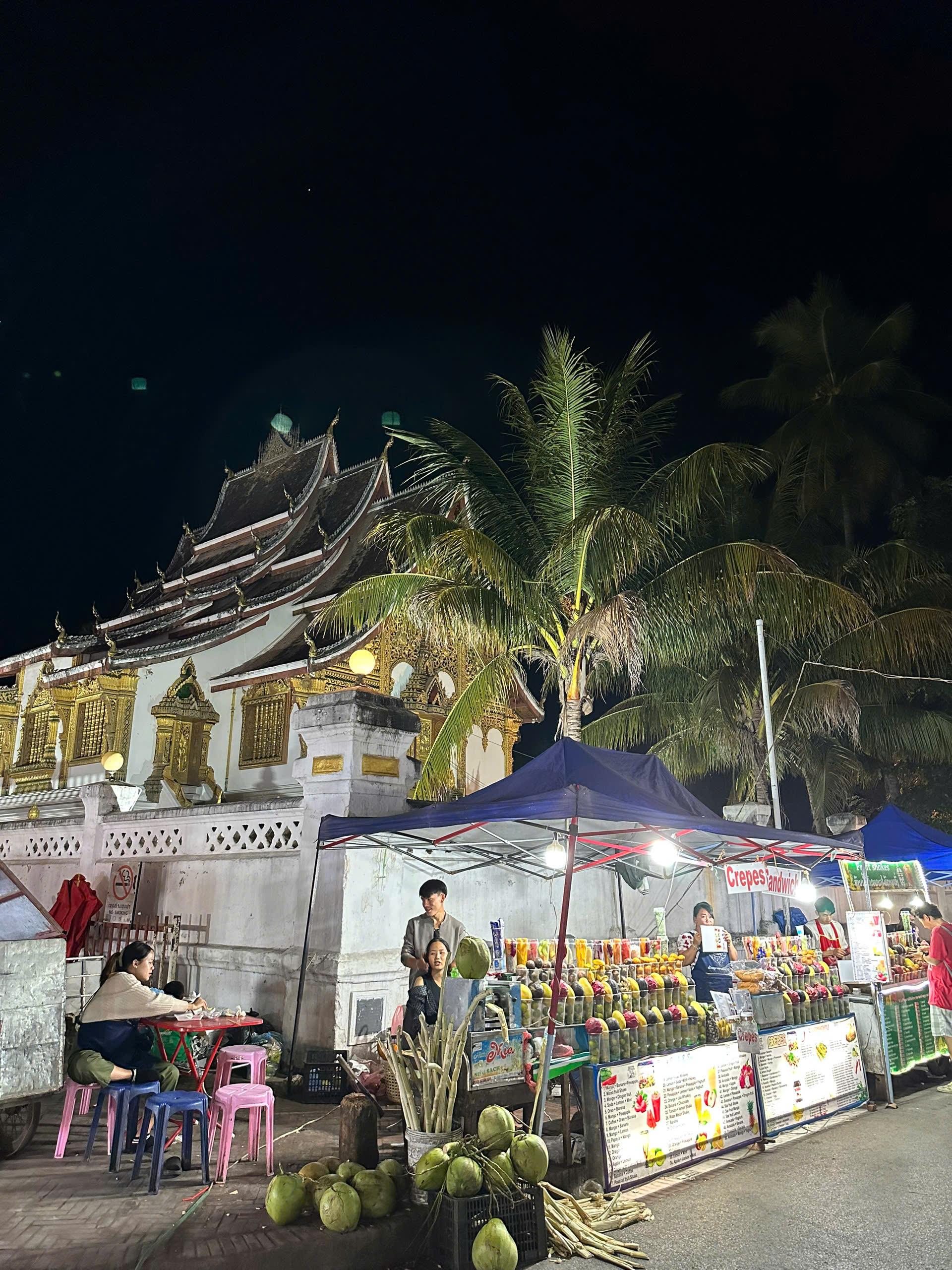 A night market with food stalls in front of a lit temple