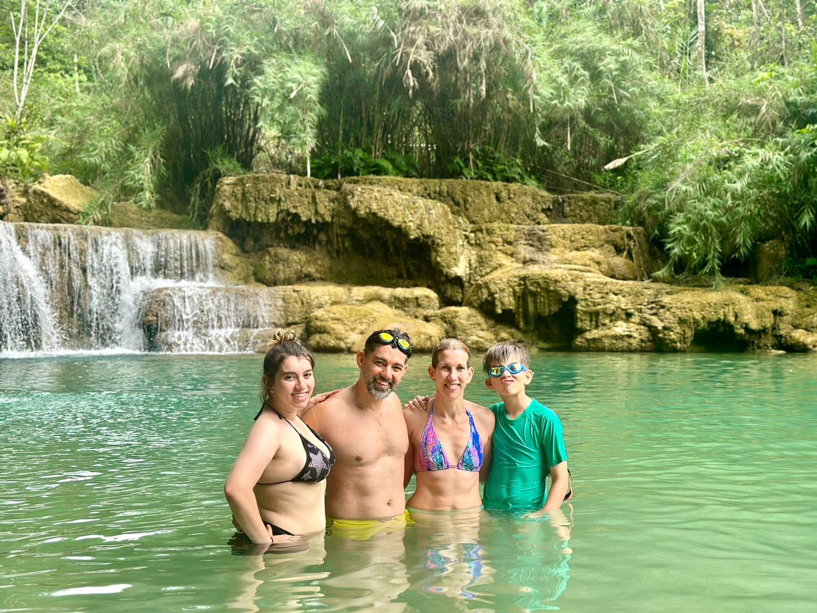 A family of four standing in the turquoise pool below a tiered waterfall