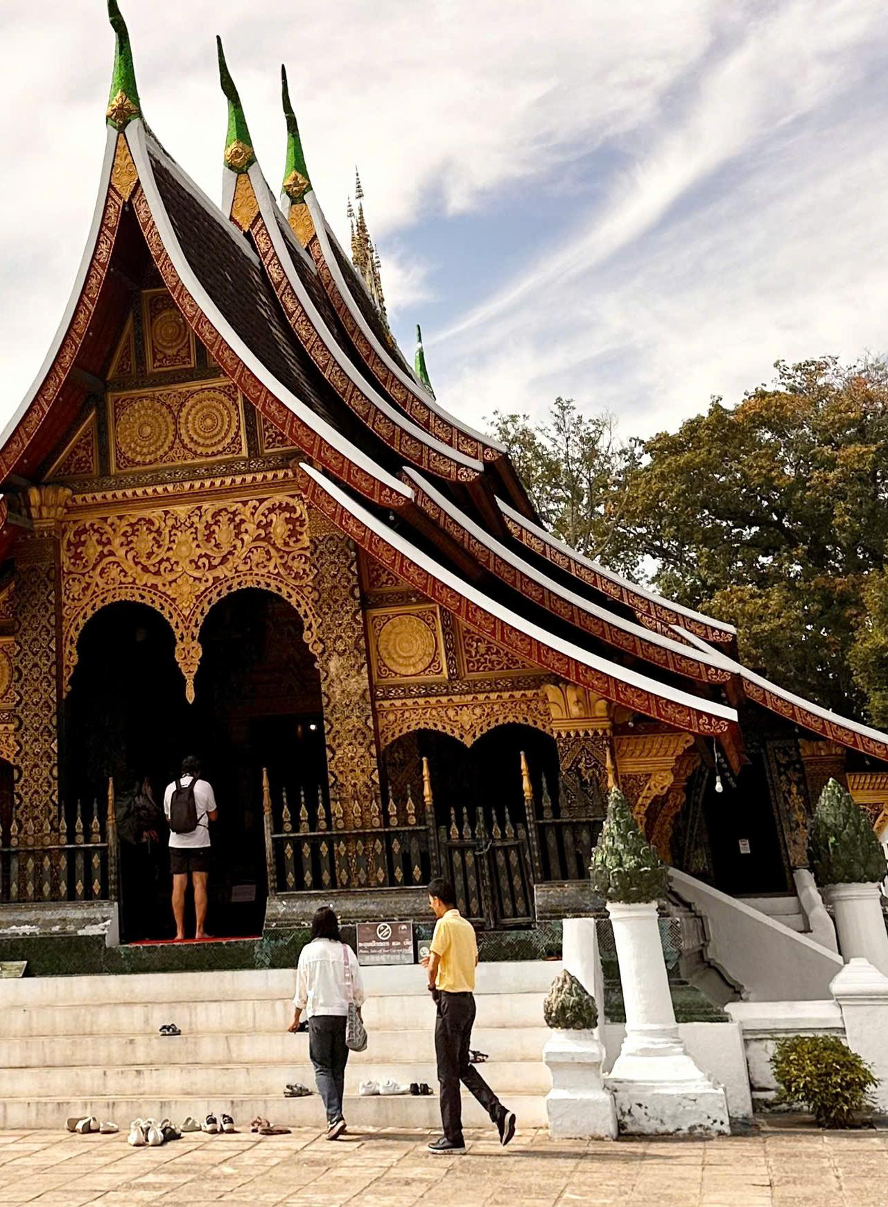 Visitors at the gilded facade of a temple with a sweeping tiered roof
