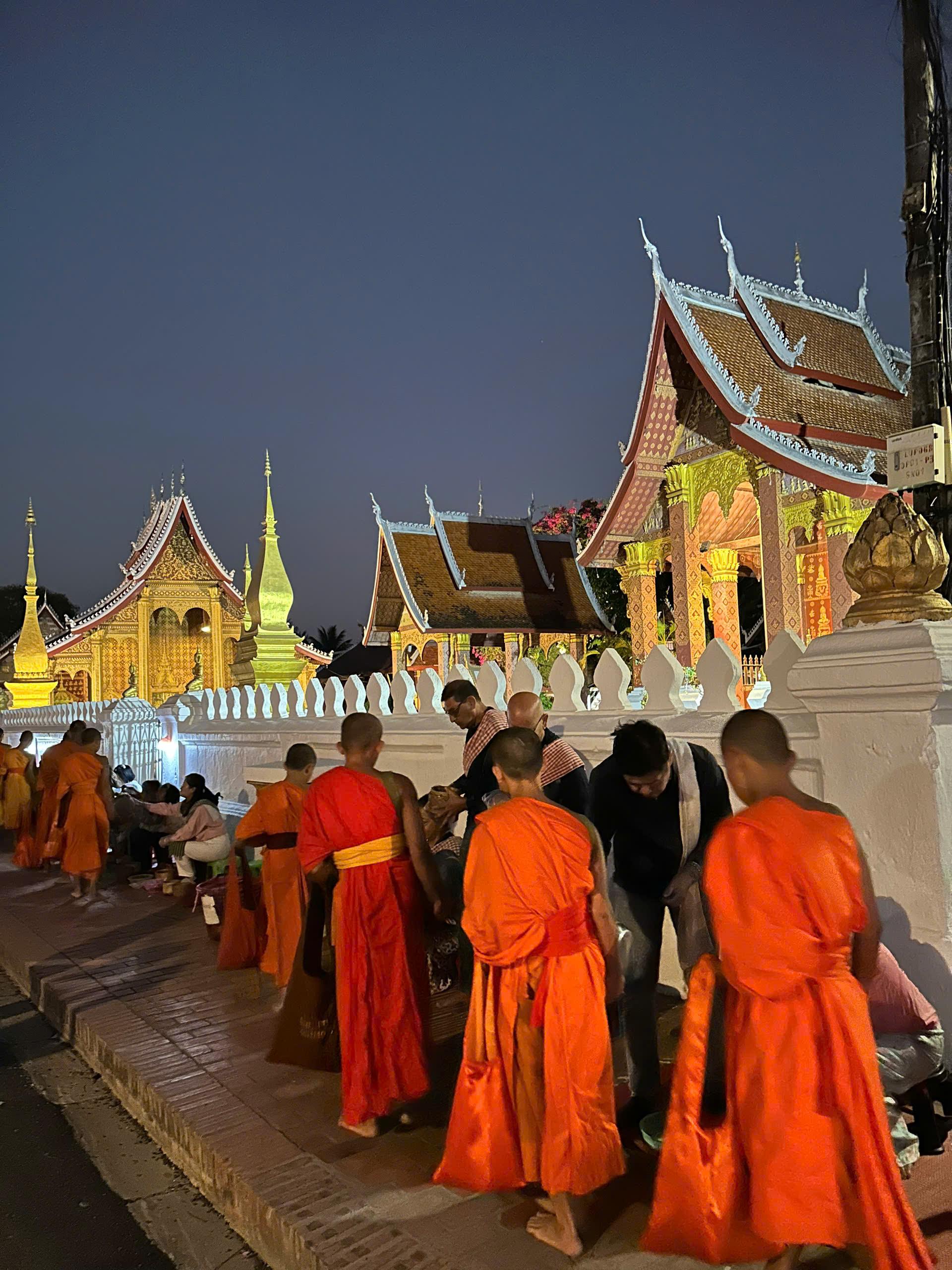Monks in orange robes gathered outside a gilded temple at night