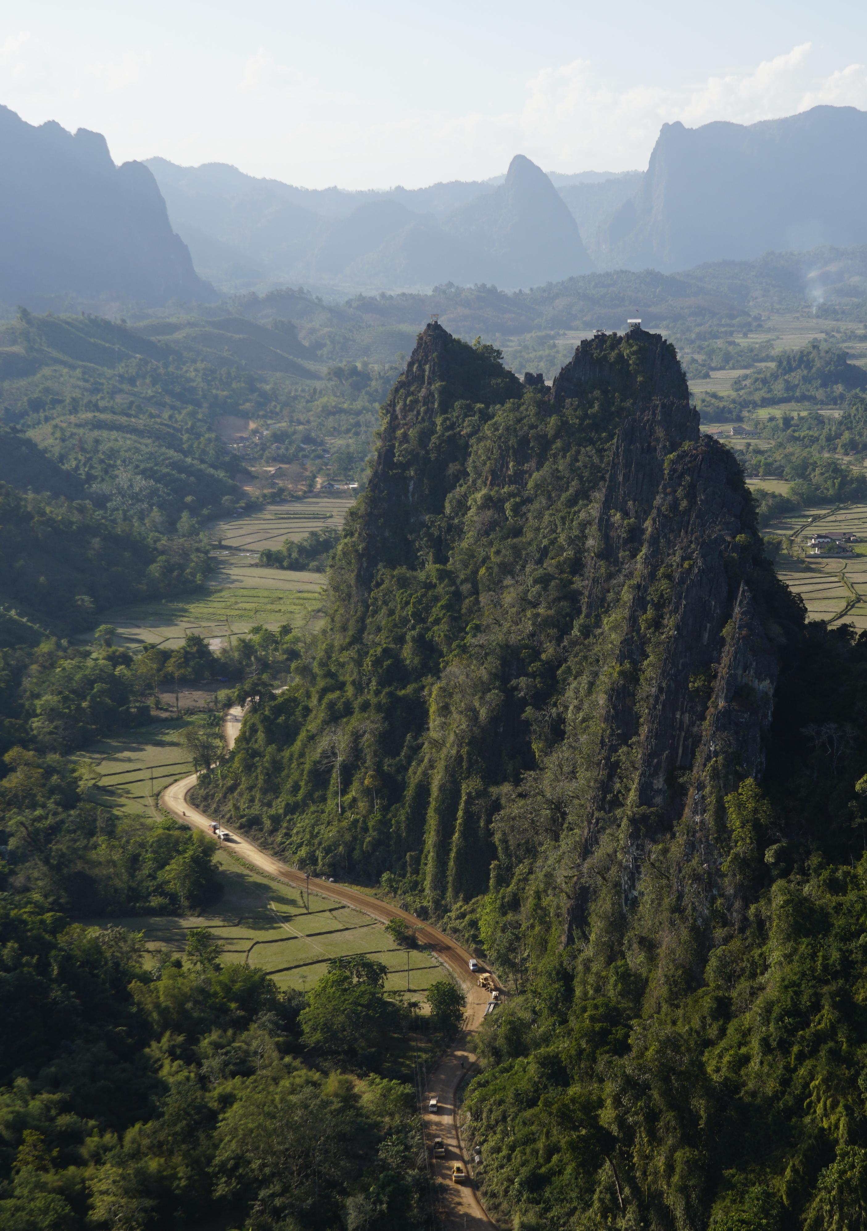 A road winding past a limestone crag above green rice fields