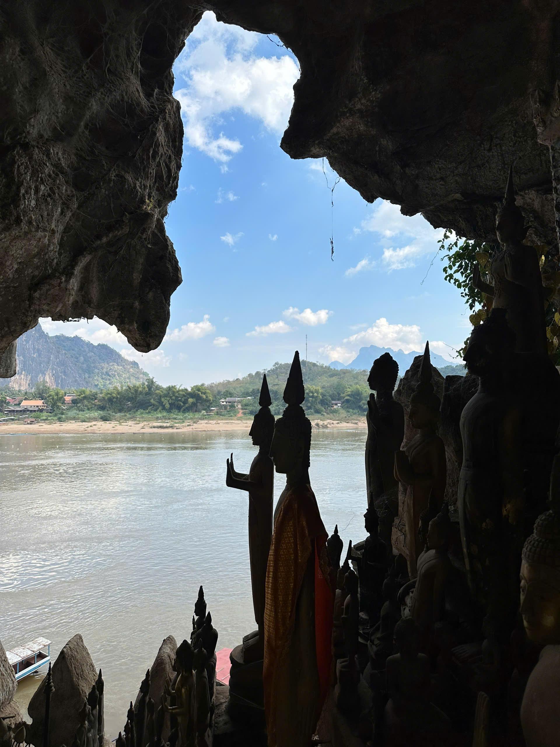 Buddha statues silhouetted in a riverside cave looking out over the water