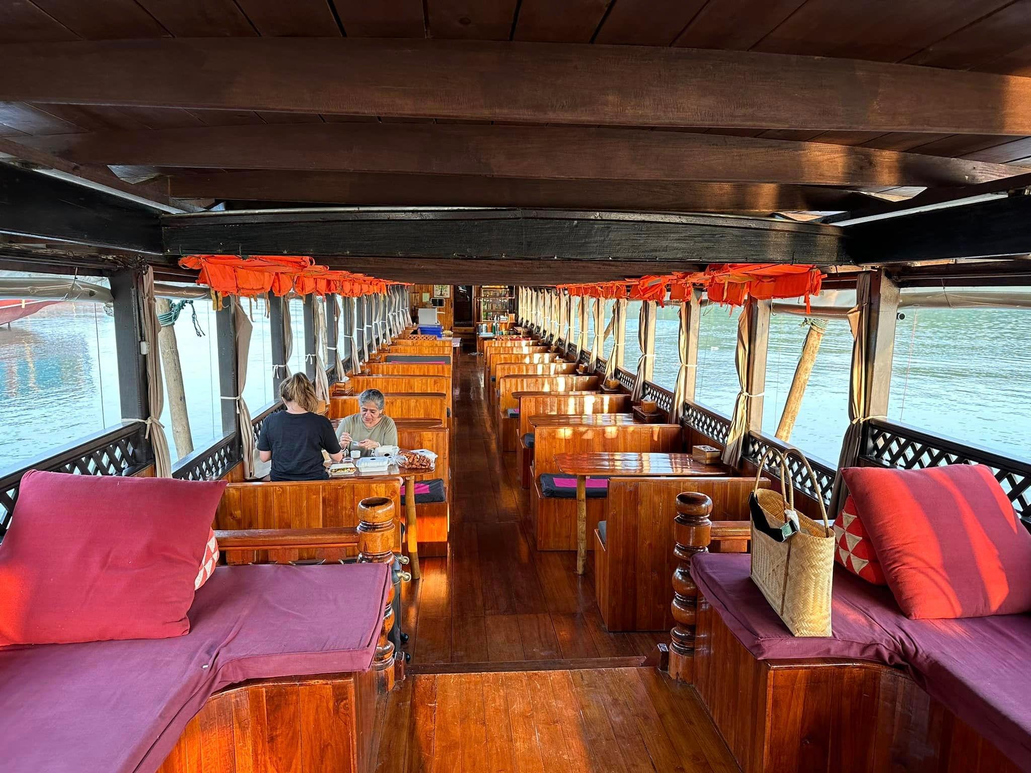 The wooden interior of a river cruise boat with rows of cushioned seats