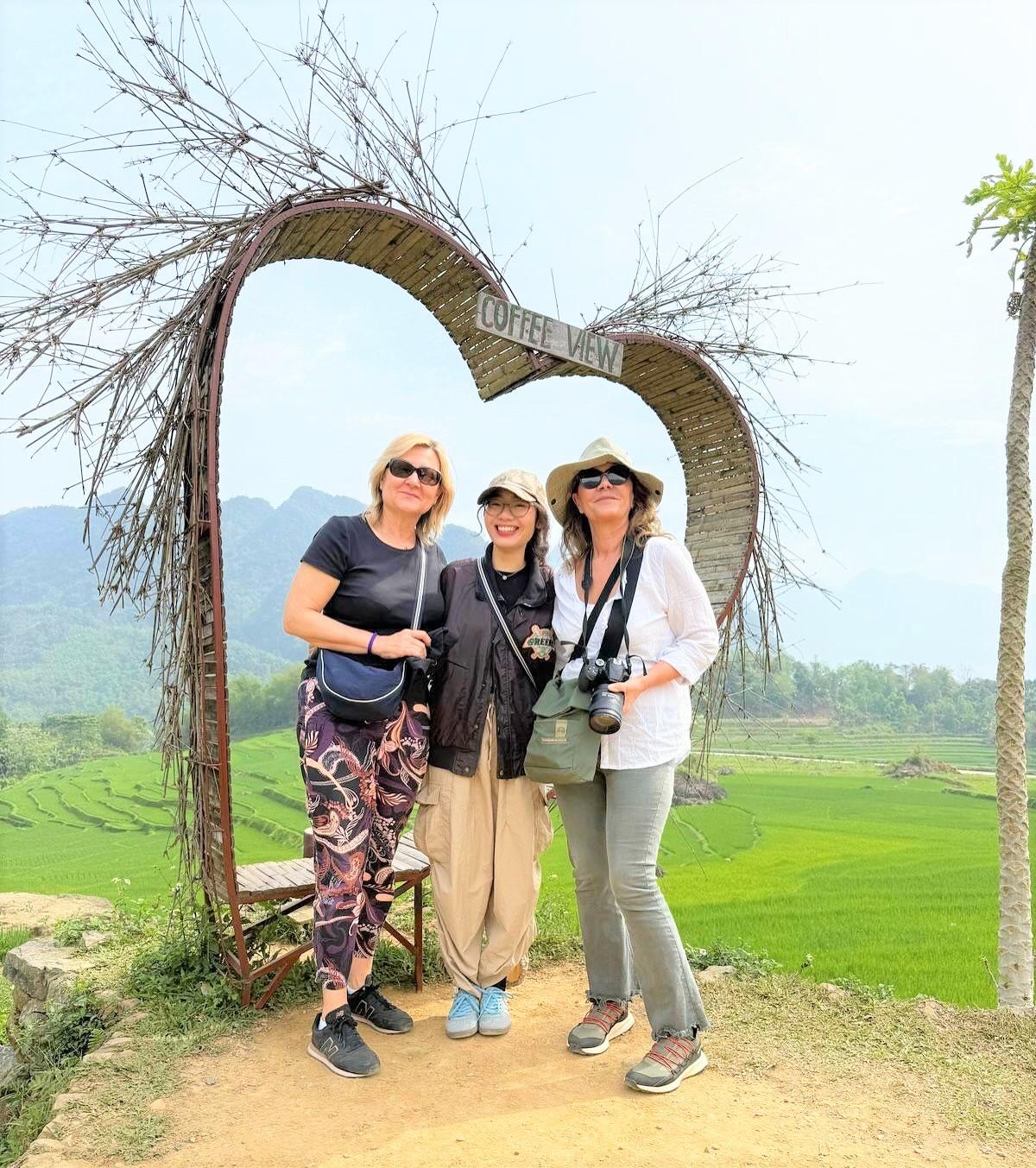 Tre viaggiatrici sotto un arco a forma di cuore, davanti alle risaie a terrazza