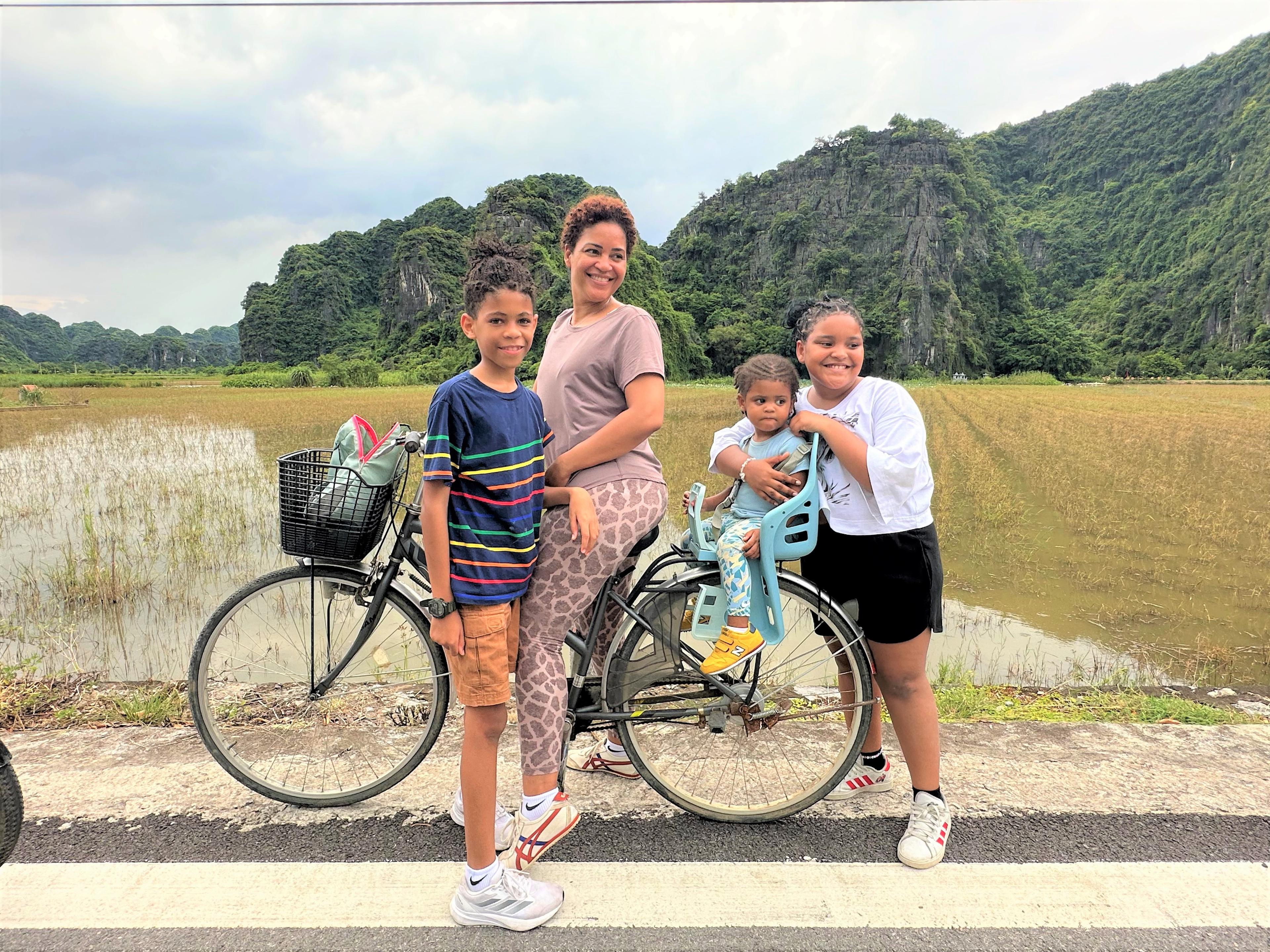 Una mamma con tre bambini e la bicicletta lungo le risaie
