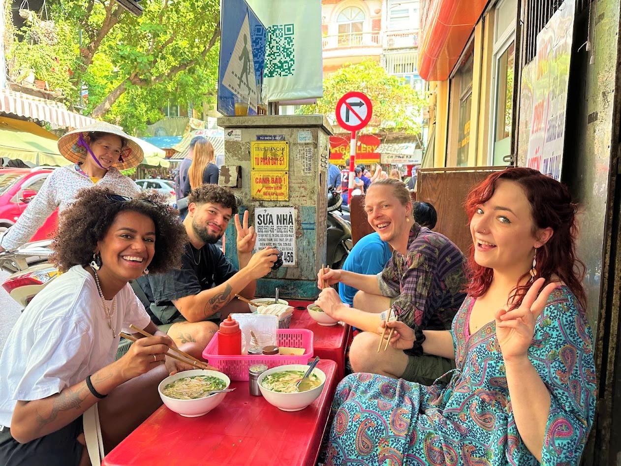 Viaggiatori a un tavolino di strada mentre mangiano il pho, ad Hanoi