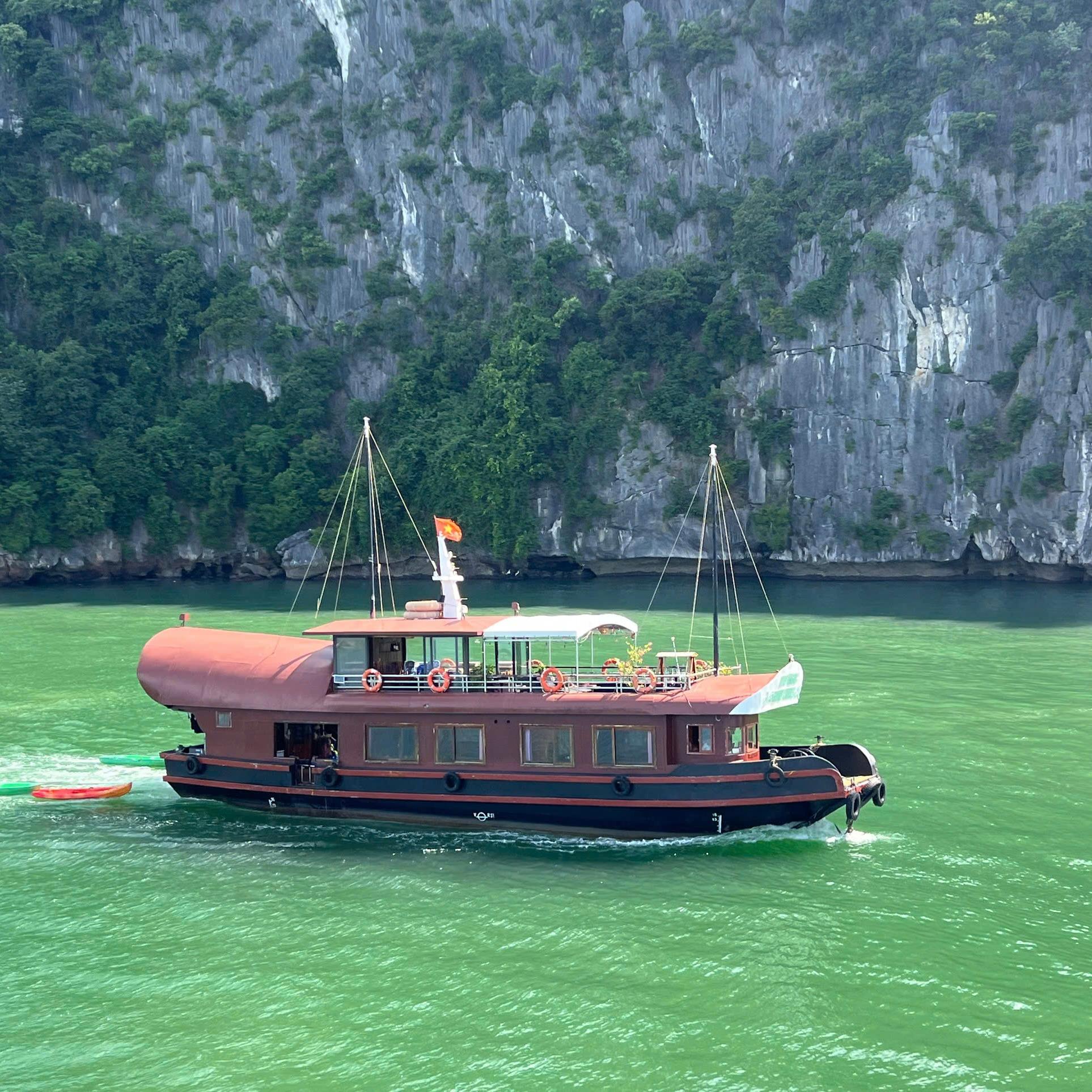 A wooden cruise boat crossing green water below limestone cliffs