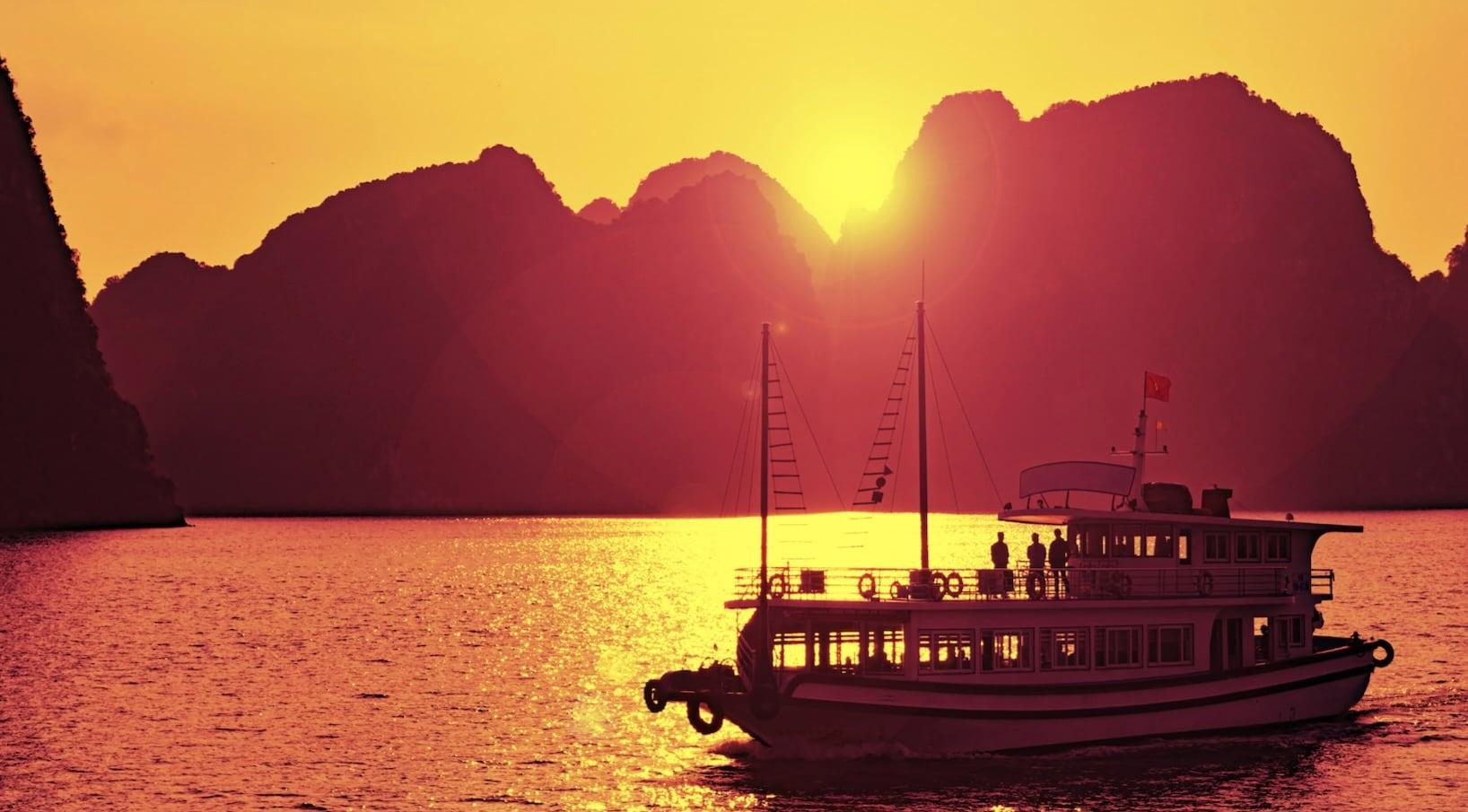 A wooden cruise boat sailing past limestone islands at sunset