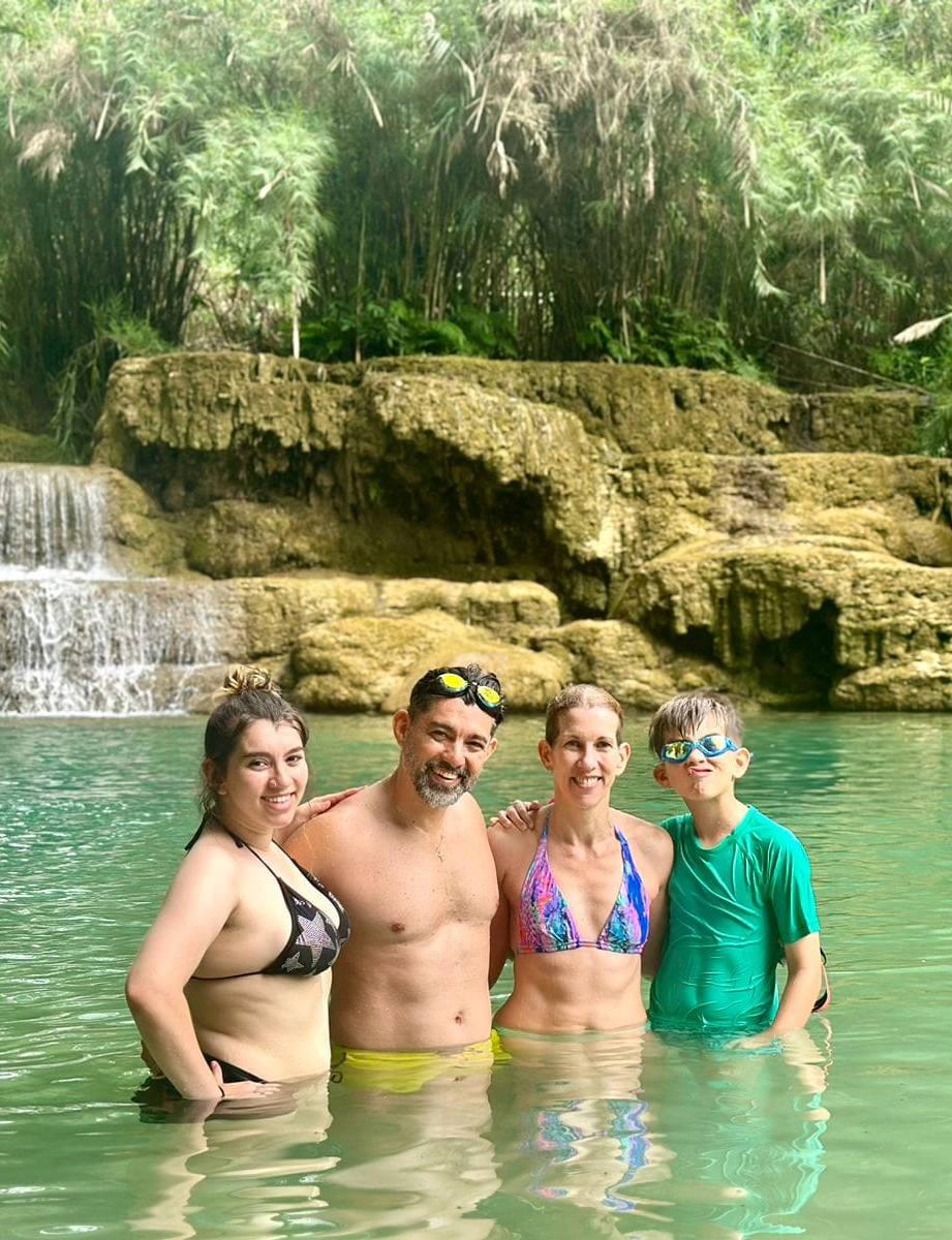 A family of four standing in the turquoise pool below a tiered waterfall