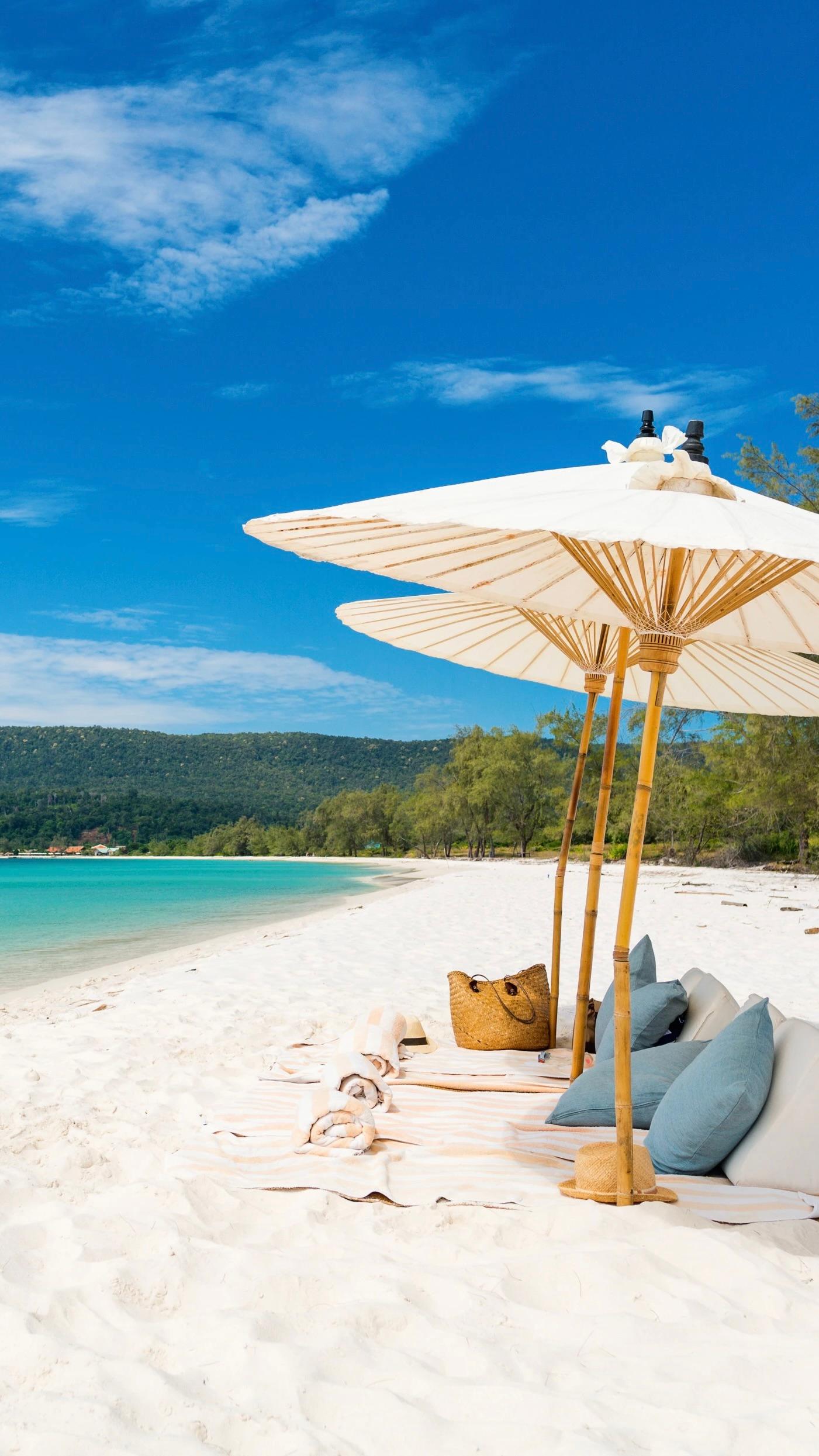 Parasols, cushions and towels set out on a white sand beach beside turquoise water