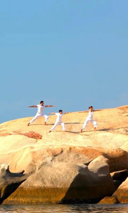 Three people in white practising yoga on granite rocks above the sea