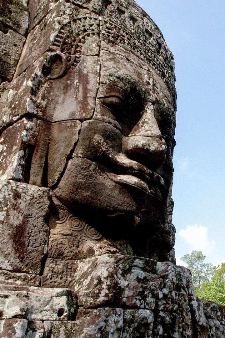 A giant stone face carved into a temple tower, seen close up against a blue sky