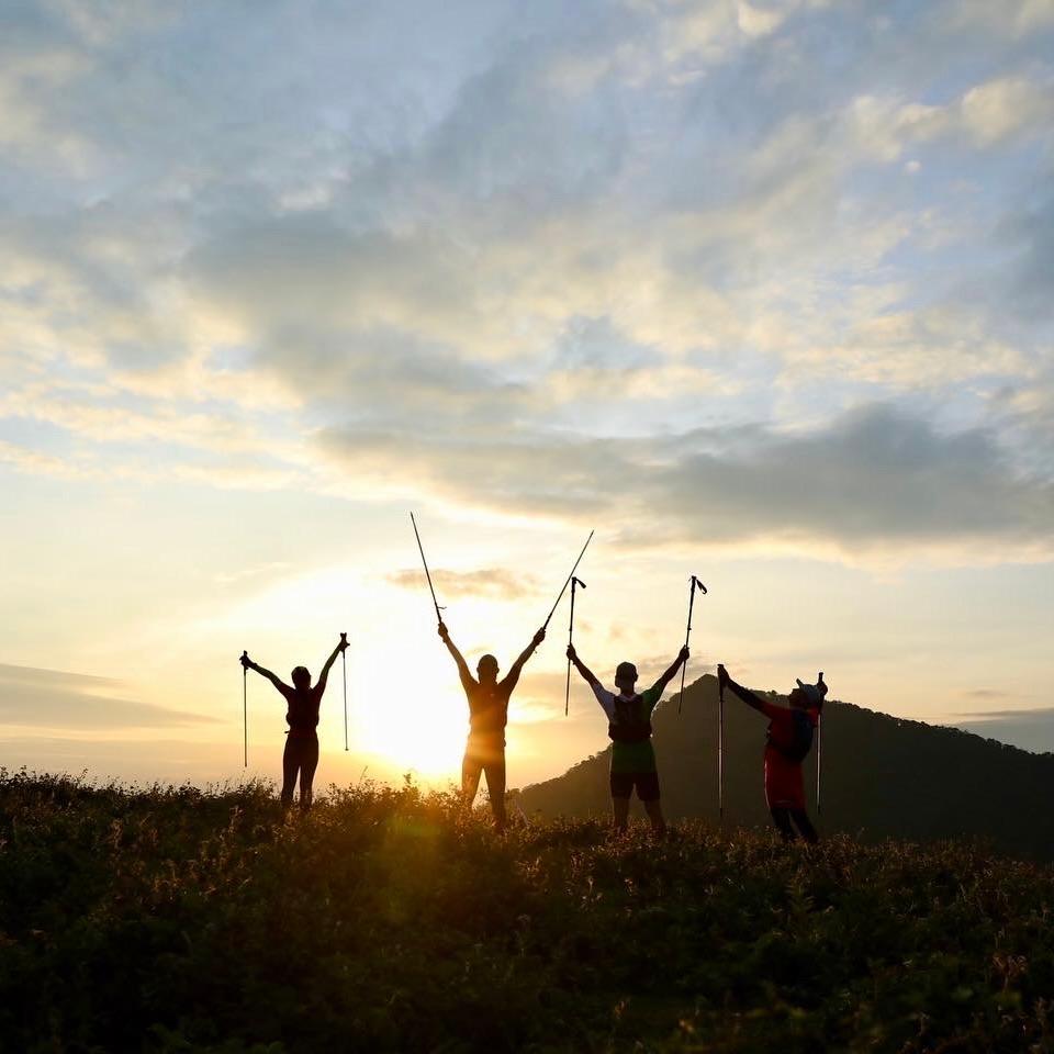 Four hikers raising their trekking poles on a hilltop at sunrise
